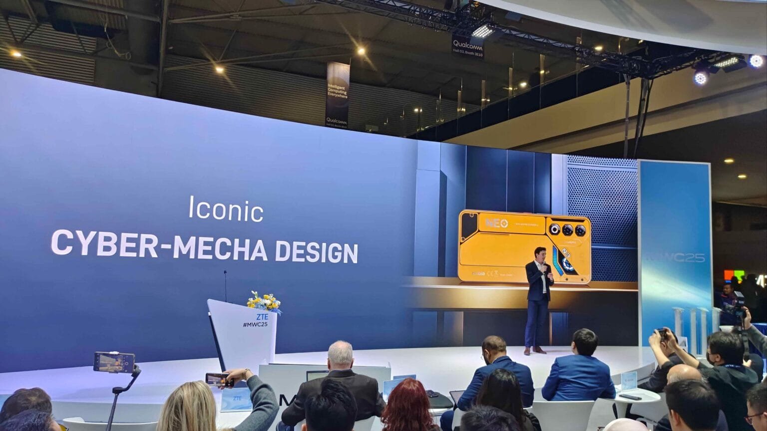 A speaker presents at the Nubia Neo 3 5G launch event during Mobile World Congress (MWC) 2025 in Barcelona, Spain. A large screen displays "Iconic Cyber-Mecha Design" and shows the Nuvia Neo 3 device. The audience is seated and some are recording the presentation with their phones. The overall atmosphere is one of a technology product launch.