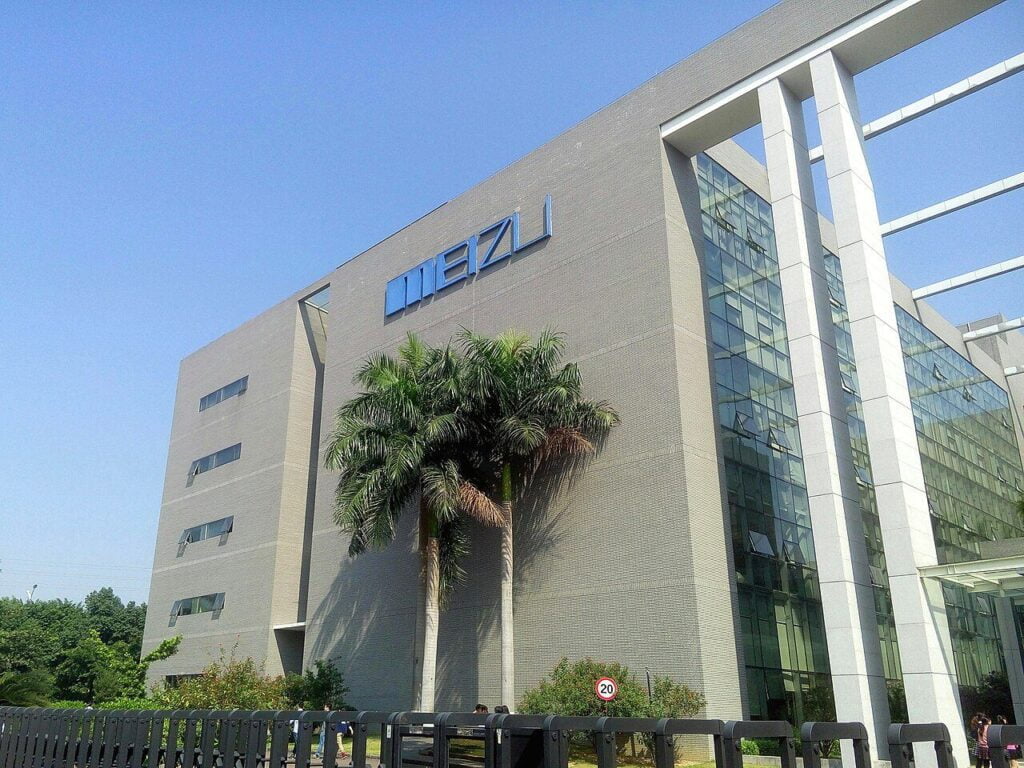 A modern building with MEIZU logo and a palm tree in front of clear blue sky.