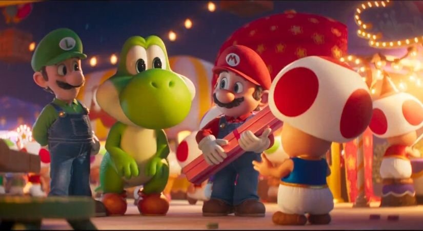 Mario holds a pink gift box while talking with Toad at a festive outdoor fair, as Luigi and Yoshi stand nearby under warm string lights in the Super Mario Galaxy movie.