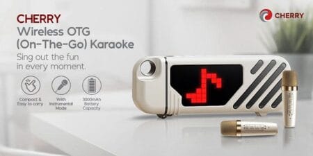 Product shot of the CHERRY Wireless OTG (On-The-Go) Karaoke machine. The device is light beige/gold, compact, and rectangular with a red LED musical note display. Two gold wireless microphones are included. Features highlighted include portability, a 3000mAh battery, and an instrumental mode.