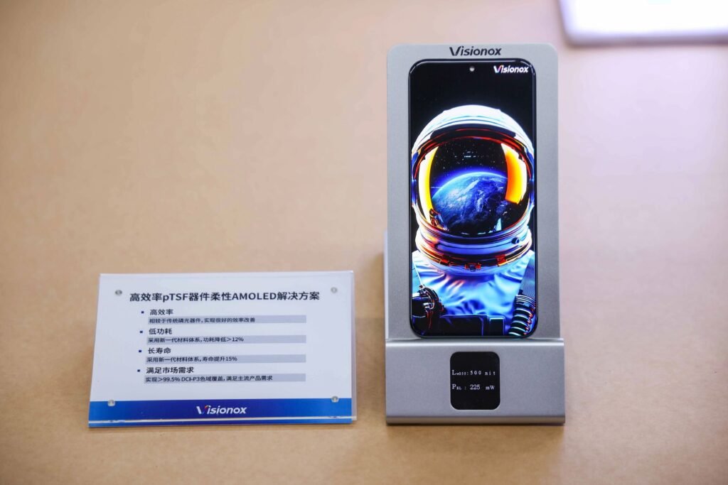 Visionox pTSF OLED display prototype showcased on a stand, showing a smartphone panel with an astronaut image and a placard highlighting high efficiency, low power consumption, extended lifespan, and wide color gamut support.