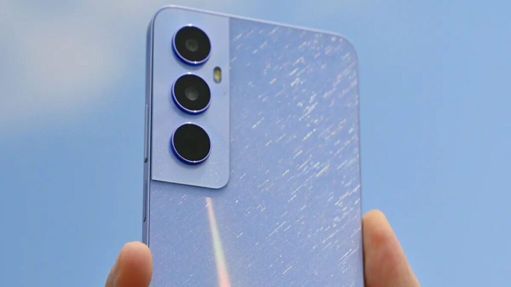 A hand holding a Realme C65 smartphone showcasing its rear camera setup against a clear blue sky.