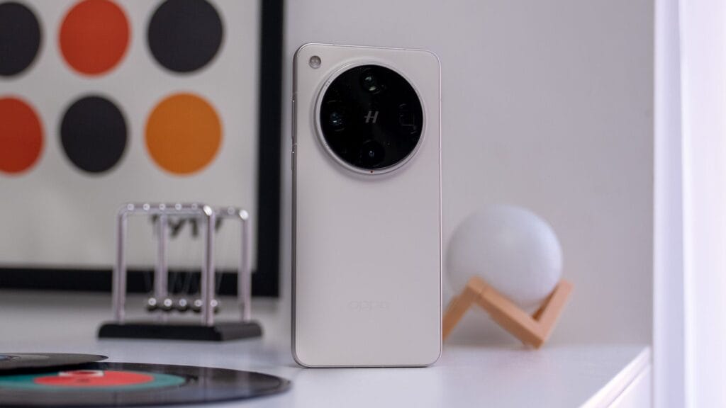 Oppo Find X8s+ with MediaTek Dimensity 9400+ and Massive 6000mAh Battery 1 Rear view of a white Oppo Find X8s+ smartphone with a circular camera module. The phone is standing on a white table with other items blurred in the background.