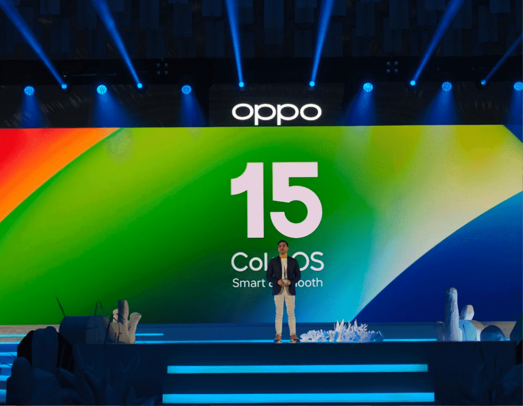 A person standing on stage at a product launch event for OPPO's ColorOS 15 operating system. The large screen behind them displays the ColorOS 15 logo.