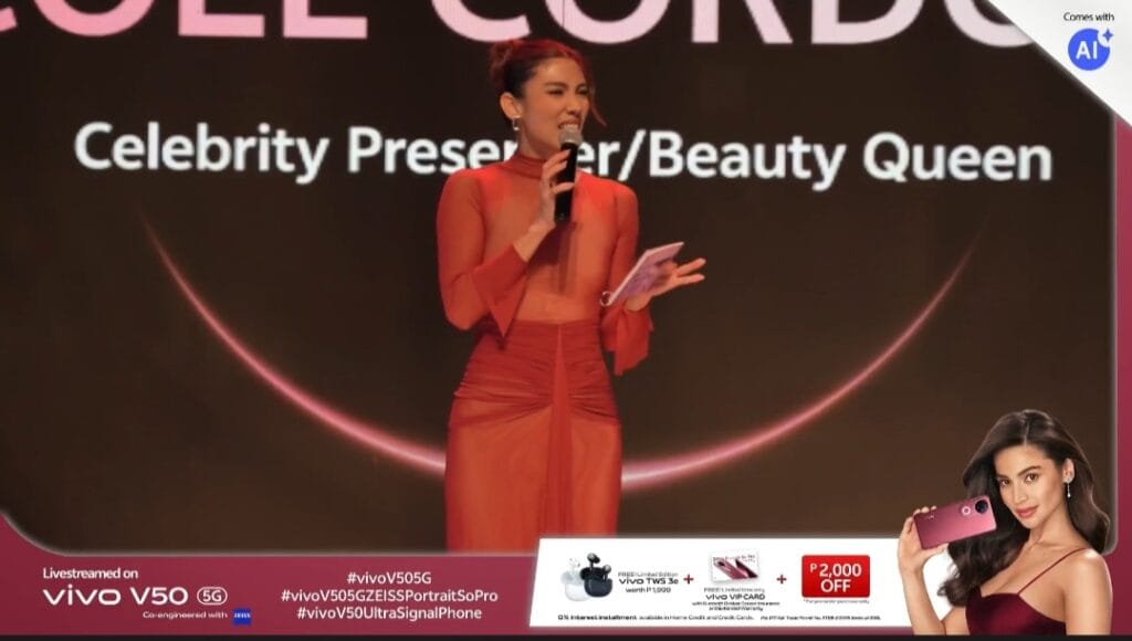 A promotional image from the Vivo V50 5G launch event in the Philippines. The image shows a celebrity presenter/beauty queen speaking on stage, holding a phone. In the lower portion, there's a smaller image of a model holding the Vivo V50 5G phone, along with promotional text detailing pre-order offers, including discounts and bundled accessories like earbuds and a VIP card. The overall image conveys the excitement and promotions surrounding the Vivo V50 5G's Philippine launch.