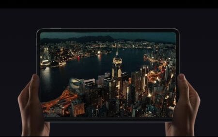 Close-up of hands holding a large Xiaomi Pad 7 Max tablet. The screen shows a vibrant aerial view of a city at night, highlighting the tablet's display quality.