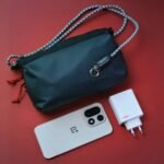OnePlus 15 Launched in China with Starting Price of CNY 3,999 4 OnePlus 15 sand dune edition on a red surface, showcasing its design alongside a charger and a stylish OnePlus crossbody bag.