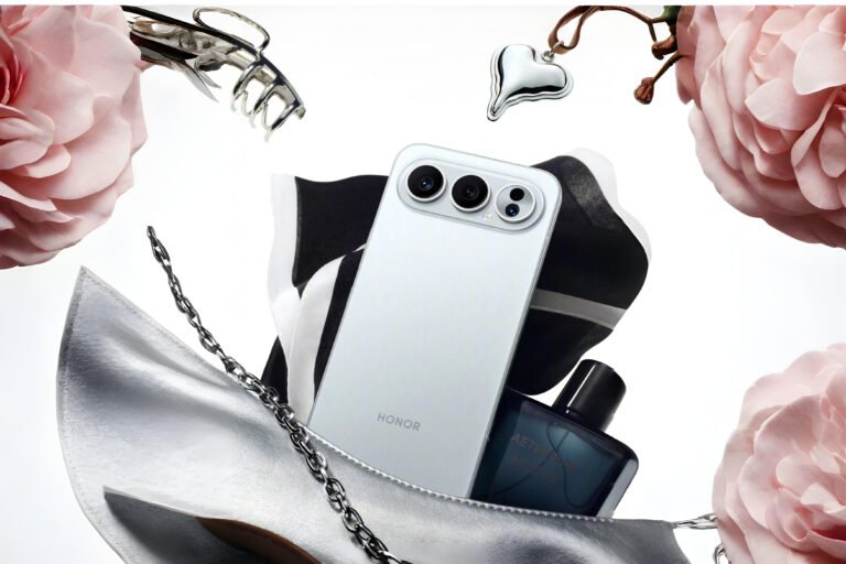 The back of a white Honor 500 Pro surrounded by roses, a silver heart pendant, a hair clip, perfume, and a silver purse.