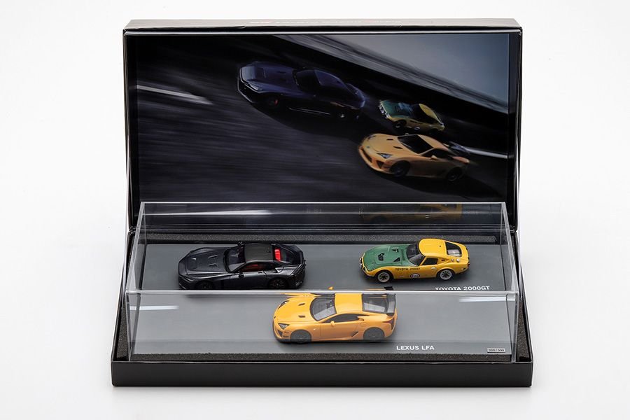 1/43 scale model three-car set from Toyota GAZOO Racing (TGR), tied to the 'THE OVERTAKE' television commercial and launching at Tokyo Auto Salon 2026. The set includes a black GR GT, green Toyota 2000GT, and yellow Lexus LFA, displayed in a sleek black case with a clear cover. The open lid features a dynamic image of the cars in motion against a blurred road background.