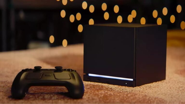 Steam Machine Price Leak Suggests Higher Cost Than Expected Ahead of 2026 Launch Black Steam Machine gaming console with a horizontal blue light strip at the base, placed next to a matching black wireless controller. Both rest on a textured light brown surface, with out-of-focus warm yellow bokeh lights in the background.