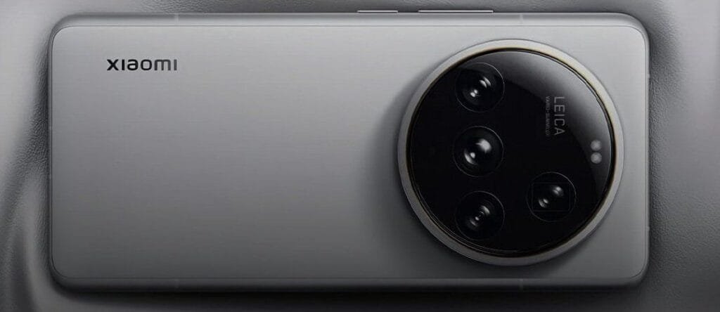 Xiaomi 15 Ultra Global Launch Confirmed by Lu Weibing 2 Close-up view of the back of a Xiaomi 15 Ultra smartphone, showcasing its circular Leica camera module with multiple lenses. The phone is silver/grey and rests on a textured surface.