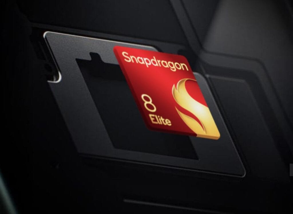 Close-up view of a Snapdragon 8 Elite processor chip being inserted into a dark-colored device. The chip is red with gold accents and the text 'Snapdragon 8 Elite' is clearly visible.