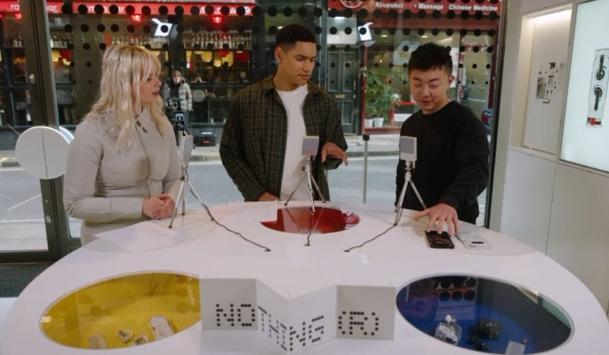 Nothing Introduces the Phone 3a Pro at MWC2025, Barcelona, Spain Three individuals are seated around a circular table at the Nothing Phone 3a Pro launch event at MWC2025 in Barcelona, Spain. The table displays the Nothing Phone 3a Pro and other related products. Each person has a microphone, suggesting a press event or interview. The background shows a city street visible through a large window.