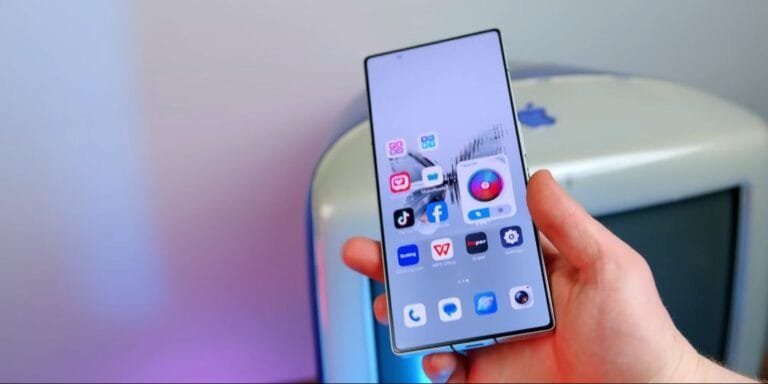 Close-up view of a hand holding the RedMagic 10 Pro smartphone. The phone's screen shows a variety of app icons, including social media and productivity apps. The background is blurred, showing a hint of a light-colored object.