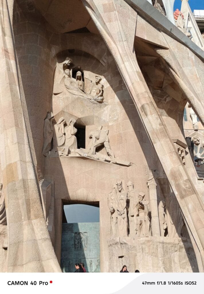 Close-up view of a section of the Sagrada Familia's facade in Barcelona, showing intricately carved stone figures depicting biblical scenes. The photo was taken with a Tecno Camon 40 Pro.