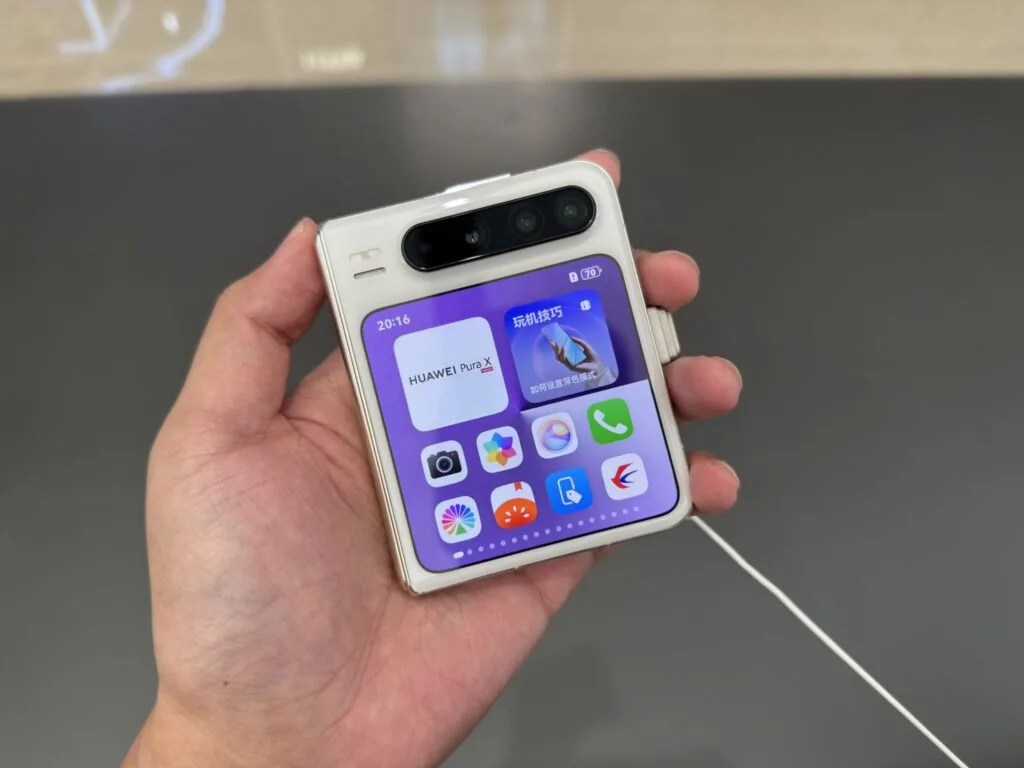 Close-up of a person's hand holding a Huawei Pura X foldable phone, showing the home screen with apps and widgets.