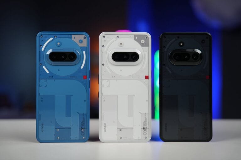 Nothing Phone 3a Launched: Starting Price at PHP 19,990 (8GB/128GB) Three Nothing Phone (3a) smartphones are displayed, showcasing their transparent backs revealing internal components. The phones are positioned side-by-side on a white surface, with a blurred background of colorful lights. The phones are in blue, white, and black.