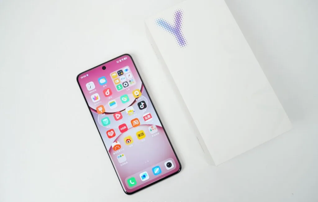 Vivo Y300 Pro+ Launched in China with a Massive 7,300mAh Battery 1 Close-up view of a Vivo Y300 Pro+ smartphone displaying its home screen with various app icons. The phone is a light pink color and is positioned next to its plain white packaging box on a white background.