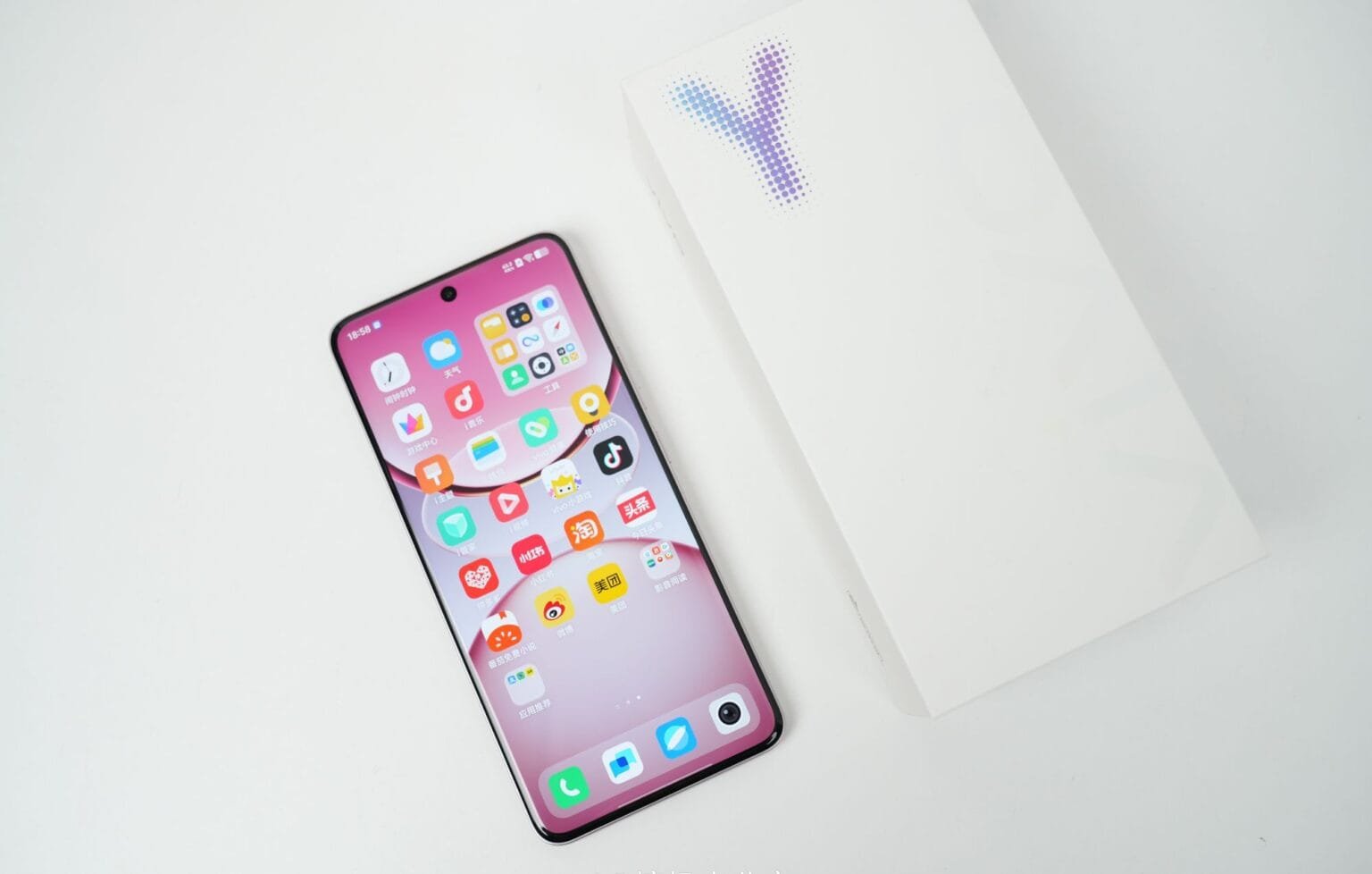 Vivo Y300 Pro+ Launched in China with a Massive 7,300mAh Battery Close-up view of a Vivo Y300 Pro+ smartphone displaying its home screen with various app icons. The phone is a light pink color and is positioned next to its plain white packaging box on a white background.