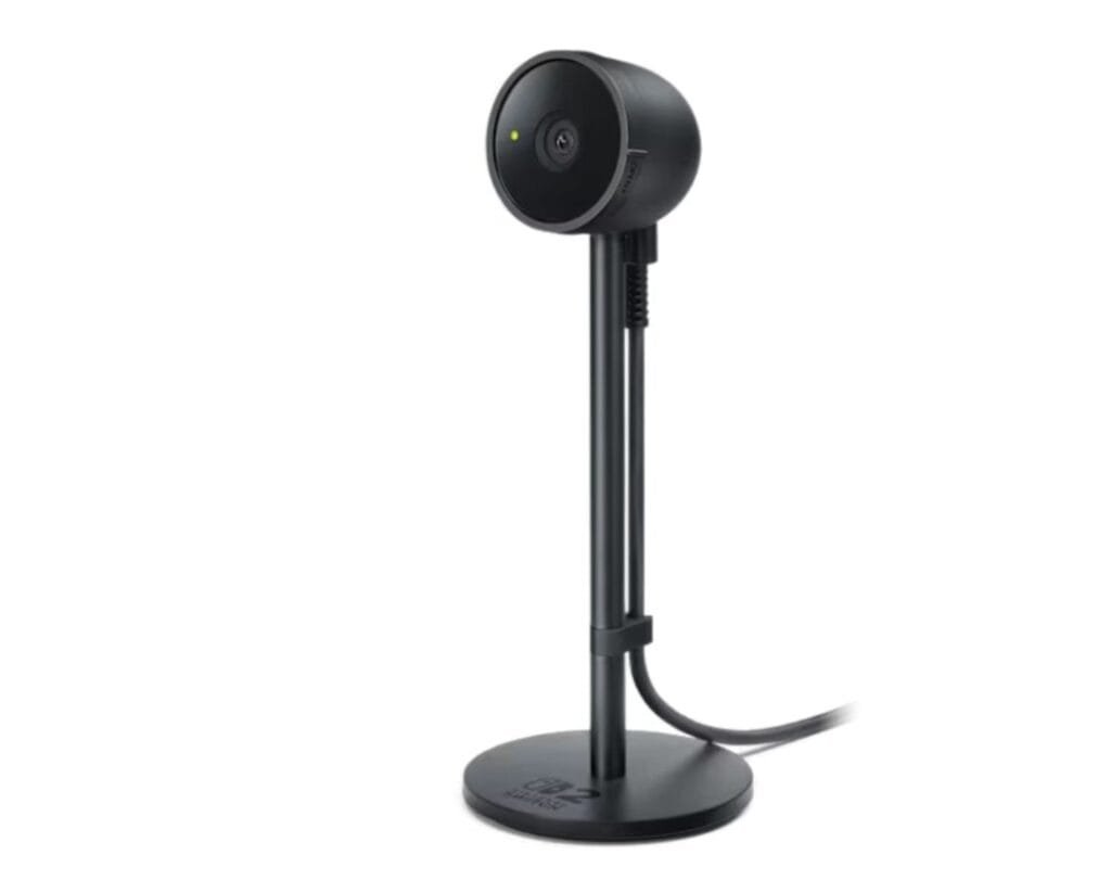 ‎A sleek, black Nintendo Switch 2 Camera sits on a circular base with a tall, slender stand. The camera lens is centrally located on the top, and a cable is visible running down the stand to the base.