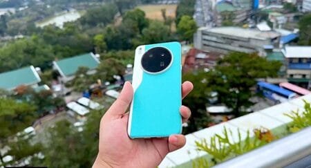 Tecno Camon 40 Premier 5G Launched in Philippines: Dimensity 8350 and 50MP Sony LYT-701 Close-up view of a hand holding the Tecno Camon 40 Premier 5G smartphone. The phone is teal with a unique circular camera module on the back. The background is blurred, showing a cityscape.