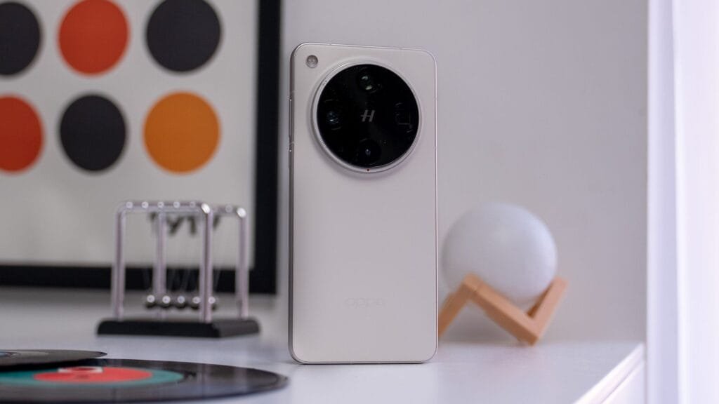 Rear view of a white Oppo Find X8s+ smartphone with a circular camera module. The phone is standing on a white table with other items blurred in the background.