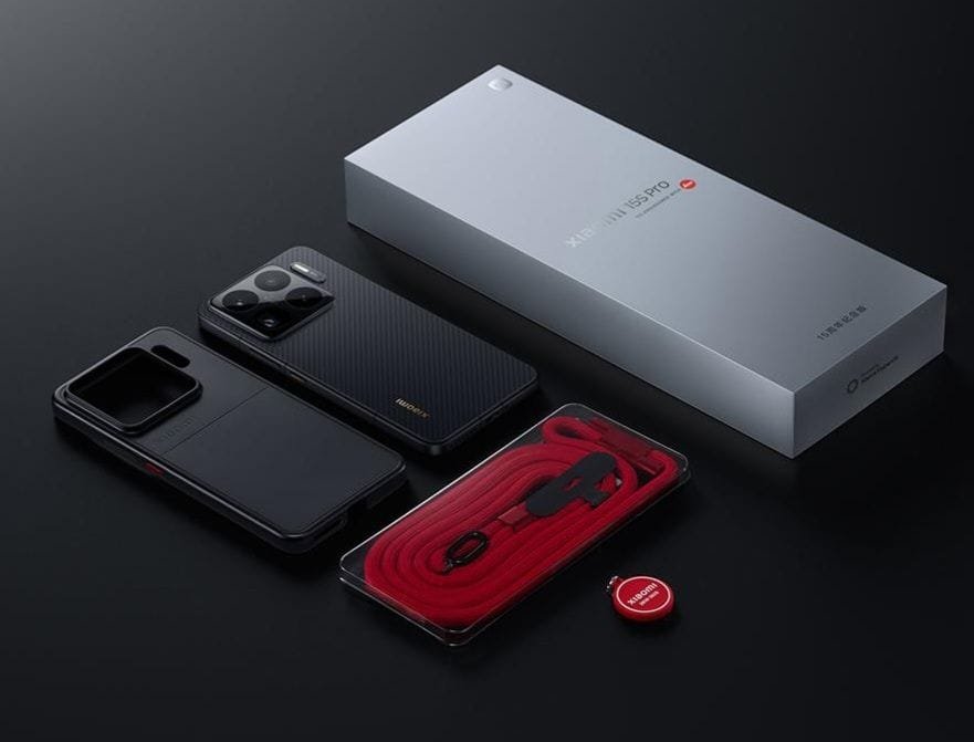 Unboxing shot of the Xiaomi 15S Pro, showing the phone, its retail box, a protective case, and a red lanyard.
