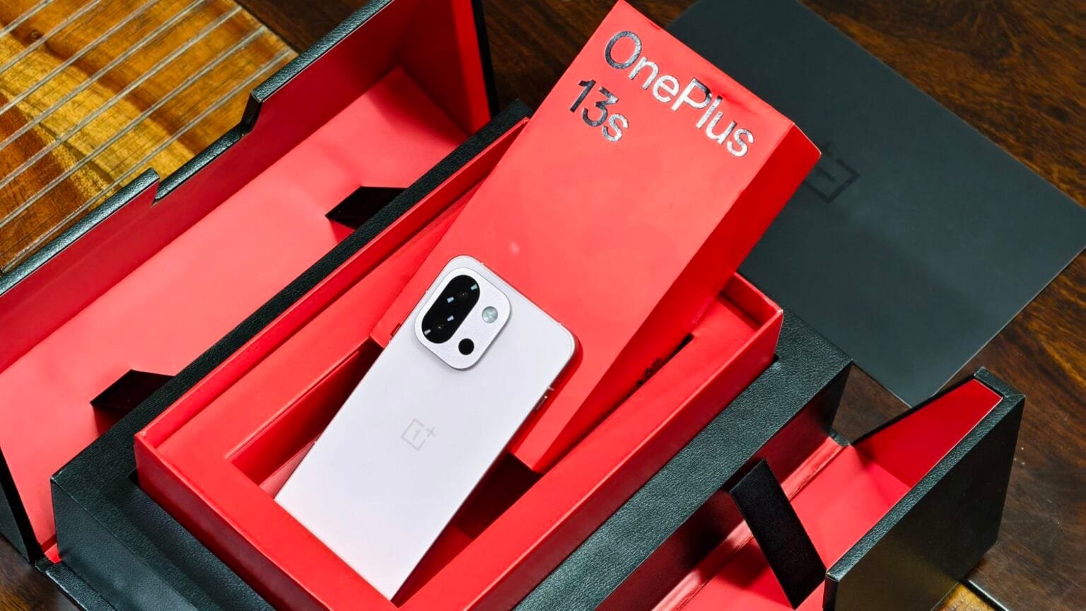 A silver OnePlus 13s indian variant smartphone rests inside a red and black retail box.