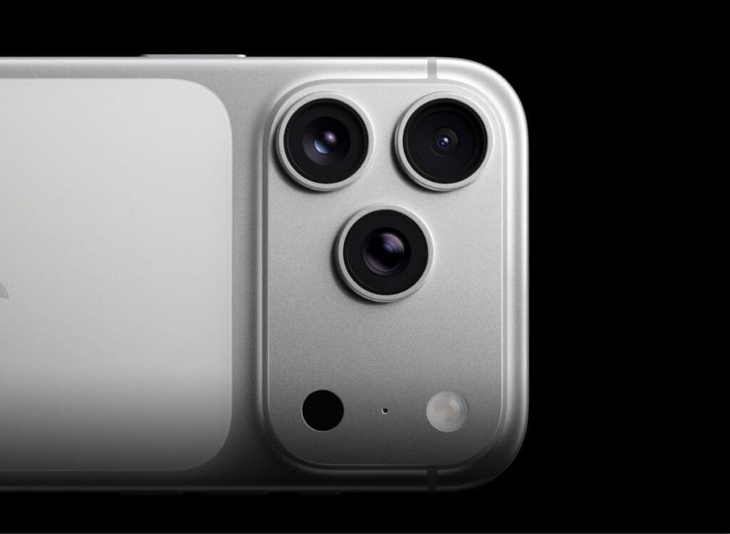 Close-up of the iPhone 17 Pro Max's silver finish with its triple-lens camera system, microphone, and flash, set against a stark black background.