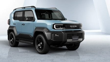 A light blue Toyota Land Cruiser FJ with black trim, featuring a boxy design, is showcased against a bright studio backdrop.