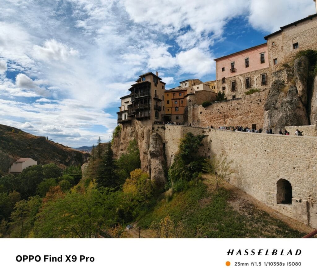 Oppo Find X9 Pro camera sample: Wide-angle shot of old buildings perched on a cliff, with trees and a cloudy sky.