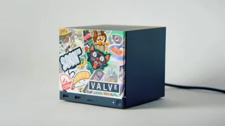 Valve Steam Machine mini PC with a cube-shaped design, featuring a front panel covered in colorful stickers and multiple USB ports at the bottom.