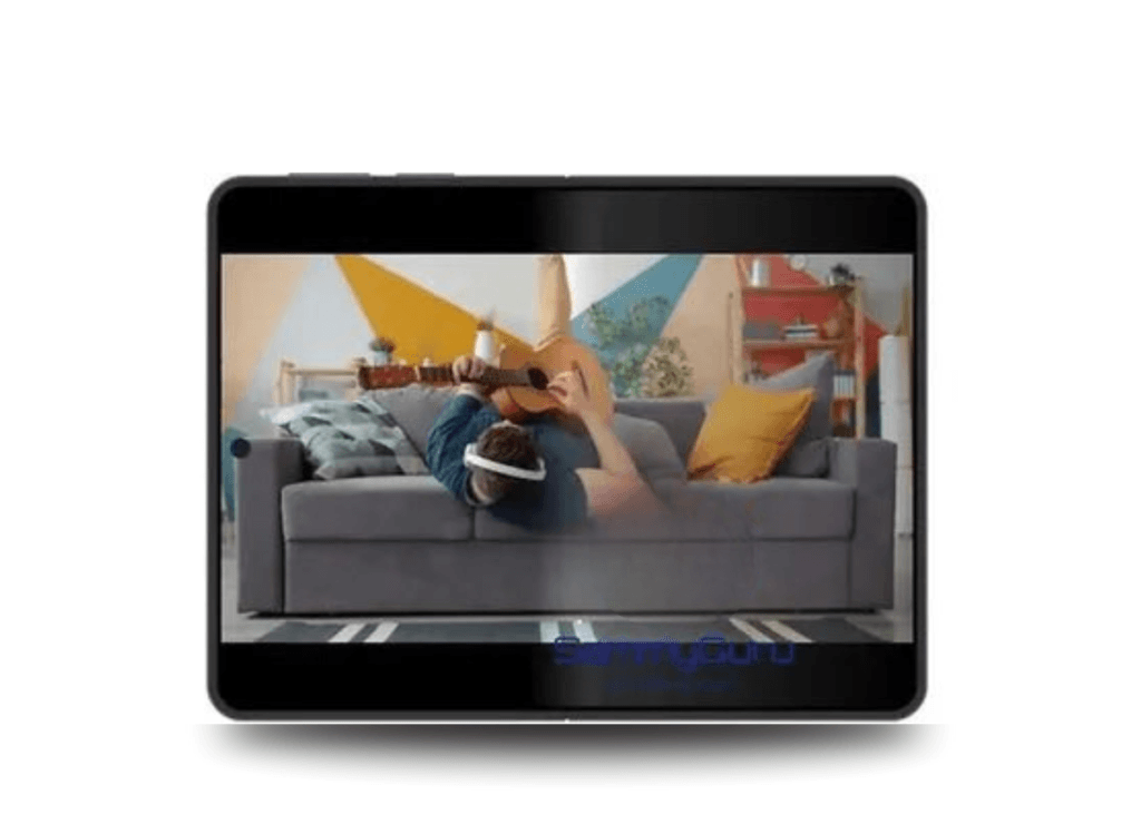 A tablet-like device, presumably the Galaxy Z Fold8, shows a video of a person wearing a VR headset, lying on a gray couch, and playing a guitar.