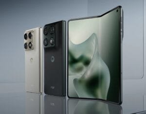 A lineup of Motorola Razr foldable smartphones displayed against a sleek, light gray background. Two closed devices are shown from the back—one in a light beige finish and the other in black with a textured surface, both featuring multi-lens camera systems and the Motorola logo along with 'razr' branding. To their right, an open Razr reveals a large, smooth foldable display with a soft green abstract wallpaper.