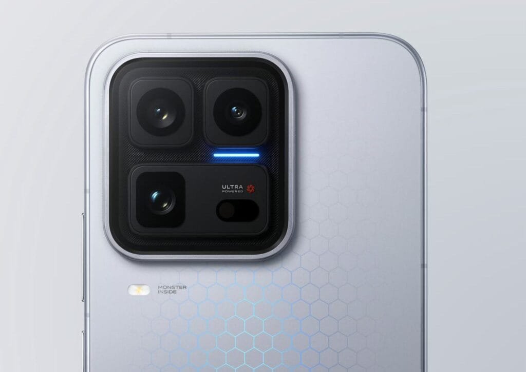 Rear close-up of the iQOO 15 Ultra smartphone in light silver. Features a large square camera module with three lenses, a blue accent light, and 'ULTRA POWERED' labeling. The back has a subtle hexagonal pattern, with 'MONSTER INSIDE' text and a flash below the module.