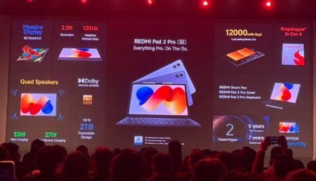 Redmi Pad 2 Pro Launched in India: Price, Specifications, Sale Details Photo from REDMI Pad 2 Pro 5G launch event – large screen shows the tablet with tagline "Everything Pro. On The Go." Key specs: 30.73cm (12.1") 2.5K 120Hz display, Snapdragon 7s Gen 4, 12000mAh battery, quad speakers with Dolby Vision-Atmos, 33W fast/27W reverse charging, up to 2TB expandable storage. Accessories include smart pen, cover, keyboard. Software: Xiaomi HyperOS with 5 years software/7 years security updates. TÜV certified. Audience visible in foreground.