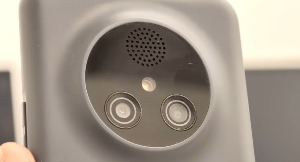 Close-up of the NexPhone's back panel, showing a large circular camera module set in a gray rugged frame. The module contains two camera lenses with silver rings, a small flash above them, and a perforated speaker grille at the top of the circle.