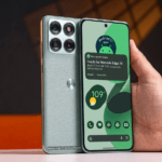 A close-up photograph of the textured teal-green back of a Motorola smartphone, featuring a square camera module with four circular lenses and the silver Motorola 'M' logo.