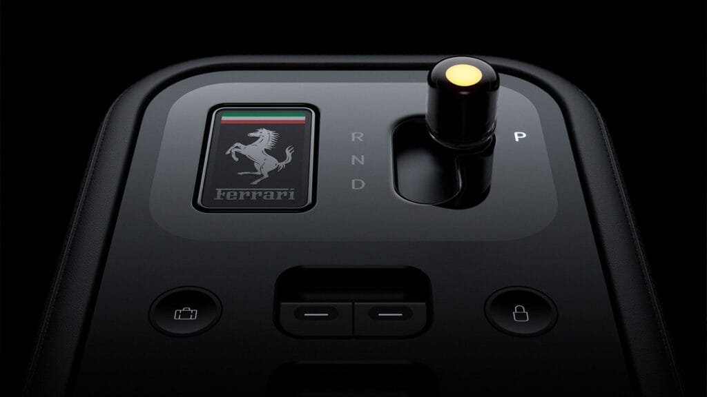 Ferrari Luce center console: Gloss black surface with embossed prancing horse badge and Italian flag accent. Features a rotary gear selector (P/R/N/D markings) and physical buttons for storage release and door locks, with premium leather trim surrounding the panel.