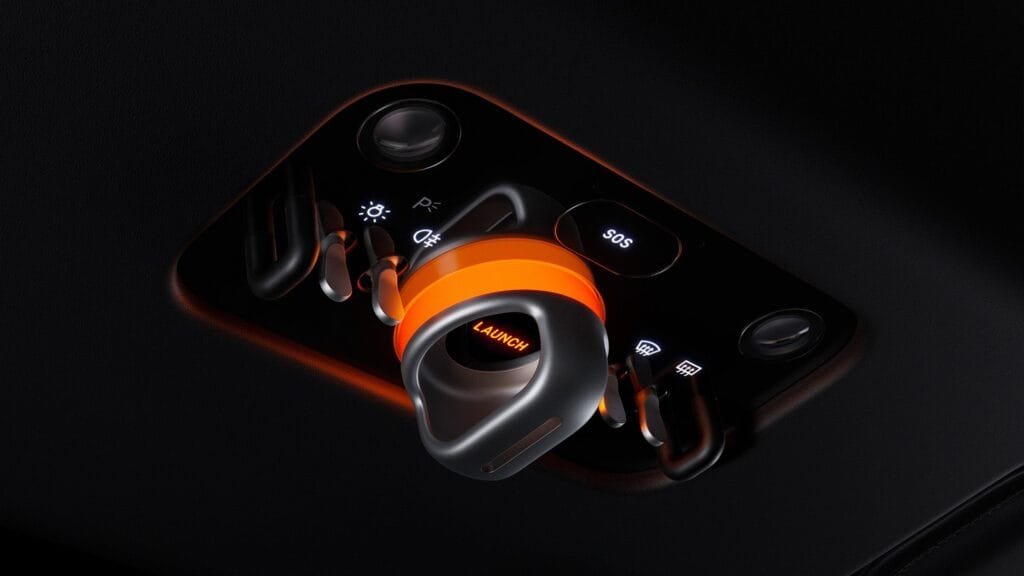 Ferrari Luce’s illuminated launch control button: A sculpted metal and orange-accented toggle labeled 'LAUNCH,' set within a black panel with adjacent controls for lights, SOS, and driver aids. The orange backlighting emphasizes the performance-focused design.