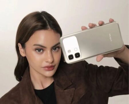 Infinix Note 60, Note 60 Pro, and Note 60 Ultra Appear on Geekbench Ahead of Global Launch A woman holding the Infinix Note 60 Pro smartphone, showcasing its gold back design with a rectangular camera module and dual rear cameras.
