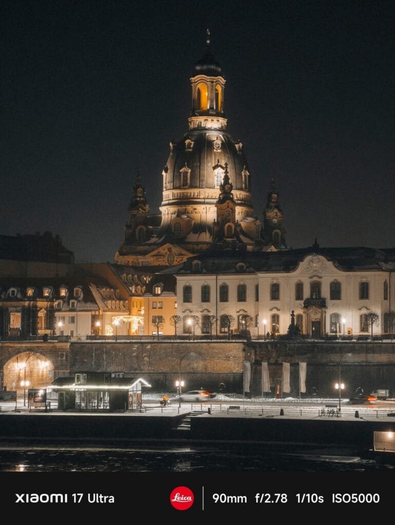 A beautiful night cityscape featuring the illuminated Frauenkirche (Church of Our Lady) in Dresden, Germany, with its distinct dome and ornate architecture. Below, city buildings line a waterfront, with reflections visible in the dark water. Snow is visible on the ground. Text at the bottom indicates "XIAOMI 17 Ultra," "Leica," and camera settings "90mm f/2.78 1/10s ISO5000.