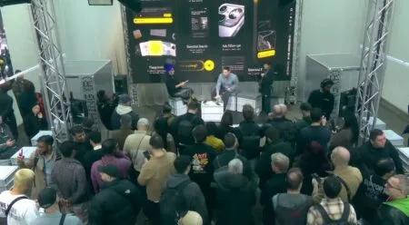 Overhead view of a product launch event of Nothing Phone 4a and Phone 4a Pro with a crowd gathered in front of a stage, where two speakers are presenting in front of a large screen displaying mobile interface graphics.