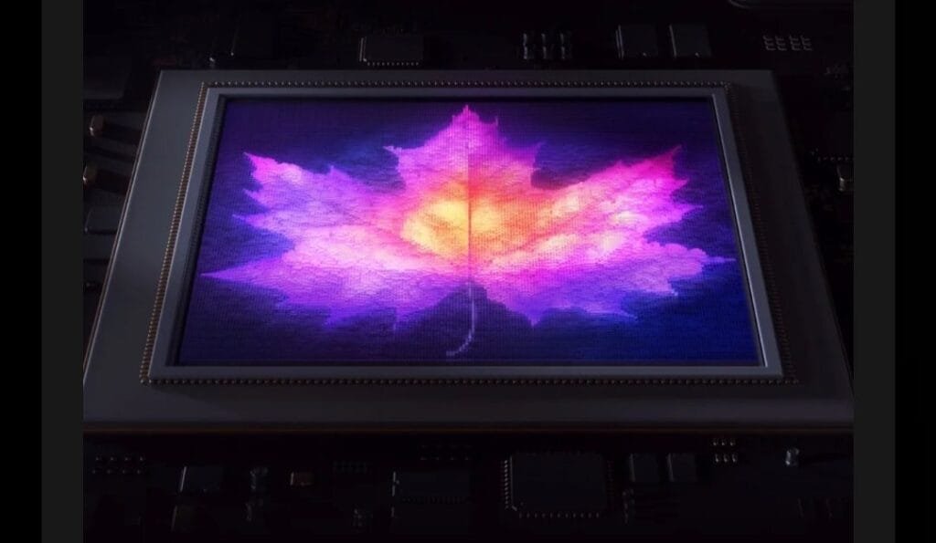 Close-up of a high-resolution display (likely from a HUAWEI device) showing a vibrant, colorful maple leaf image with gradients of purple, pink, and orange. The screen is set against a background of electronic circuit components.