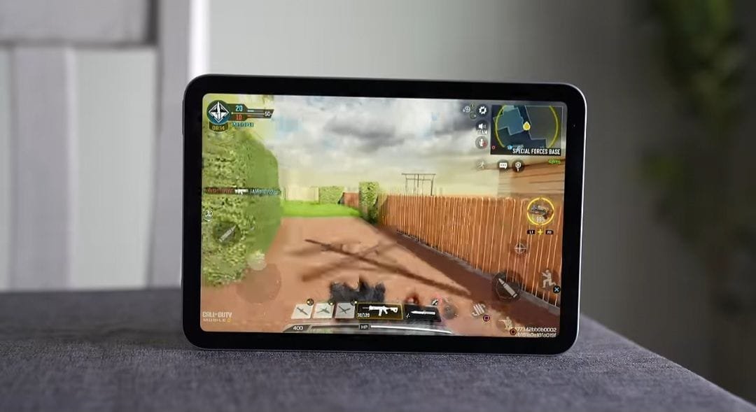 Apple iPad mini (7th generation) displaying a Call of Duty mobile game interface on its screen, showing gameplay graphics, controls, and in-game UI elements. The tablet is placed on a surface with a blurred indoor background.