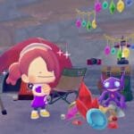 Screenshot from Pokémon Pokopia showing a female trainer character smiling beside Sableye, surrounded by colorful gemstones, treasure, and camping gear with hanging crystal decorations