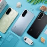 Flat-lay shot of three Redmi A7 Pro smartphones in light green, light blue, and black colorways, displayed alongside their retail box, 15W charger, USB cable, clear protective case, SIM tool, and user manual, arranged on a bright blue surface decorated with seashells and green leaves.