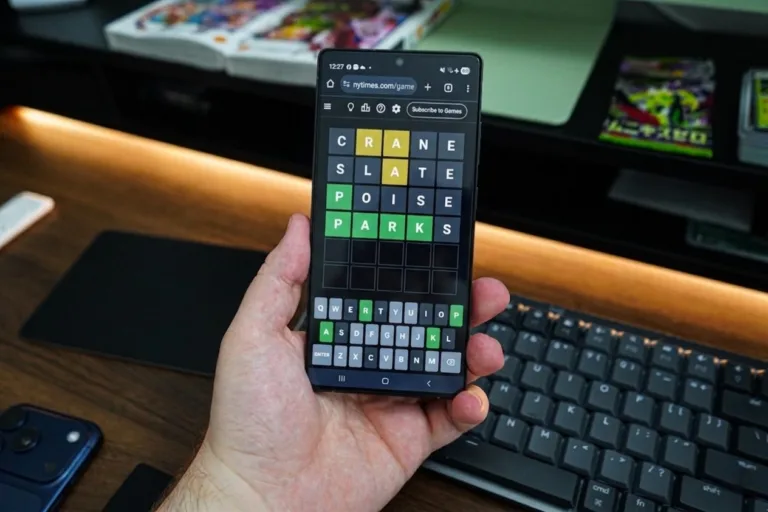Hand holding smartphone showing Wordle game on NY Times website; guesses: CRANE (A,N yellow), SLATE (A,T yellow), POISE (P green), final correct answer PARKS (all green tiles). On-screen keyboard highlights used and correct letters.
