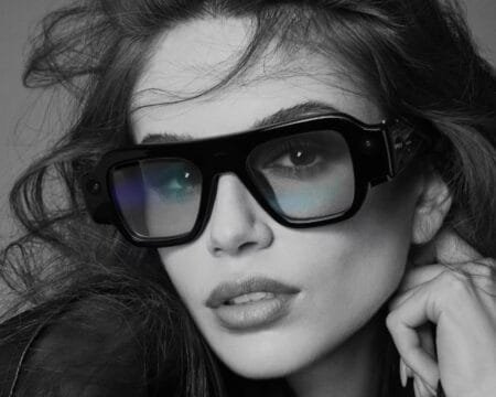 Snap SPECS AR Glasses Officially Unveiled, Priced at $2,195 Snap SPECS AR glasses shown in glossy black frame design, worn in black‑and‑white studio shot; visible camera module on side arm, bold angular silhouette, reflective lenses; modern wearable tech with stylish eyewear form factor.