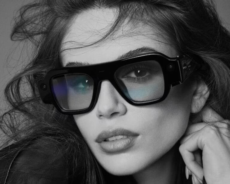 Snap SPECS AR Glasses Officially Unveiled, Priced at $2,195 Snap SPECS AR glasses shown in glossy black frame design, worn in black‑and‑white studio shot; visible camera module on side arm, bold angular silhouette, reflective lenses; modern wearable tech with stylish eyewear form factor.